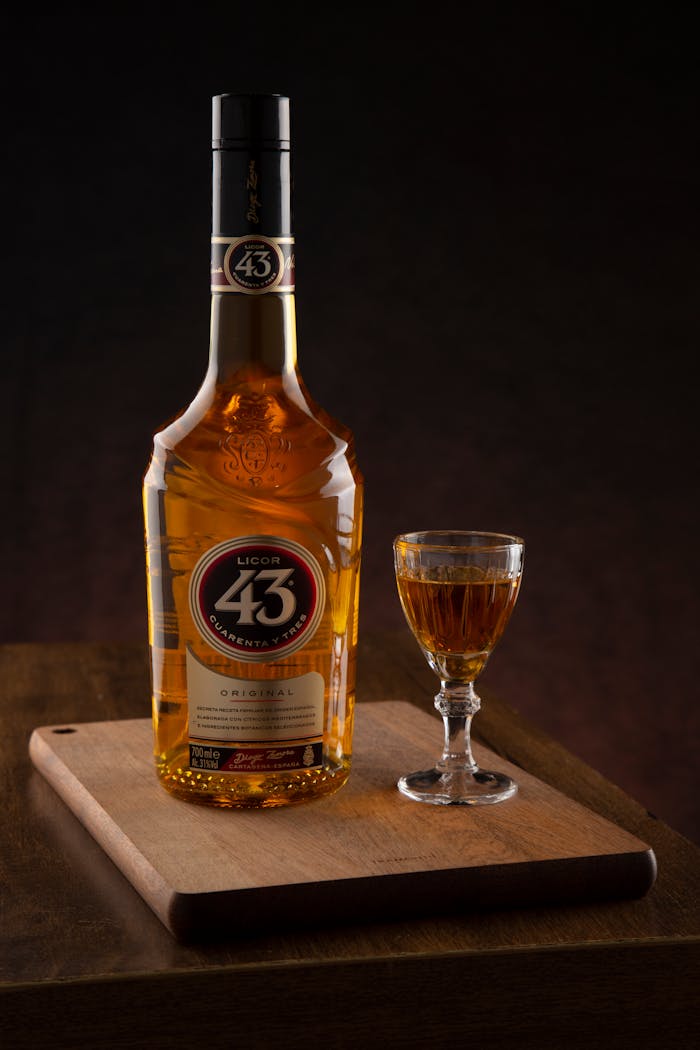 A bottle of Licor 43 and a glass on a wooden board with dark background.