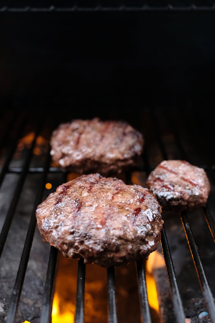Close-up of beef patties grilling over an open flame for a delicious barbecue.