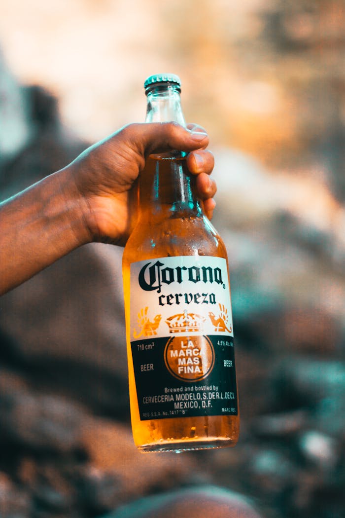 Close-up of a hand holding a Corona beer bottle outdoors, showcasing the brand label.